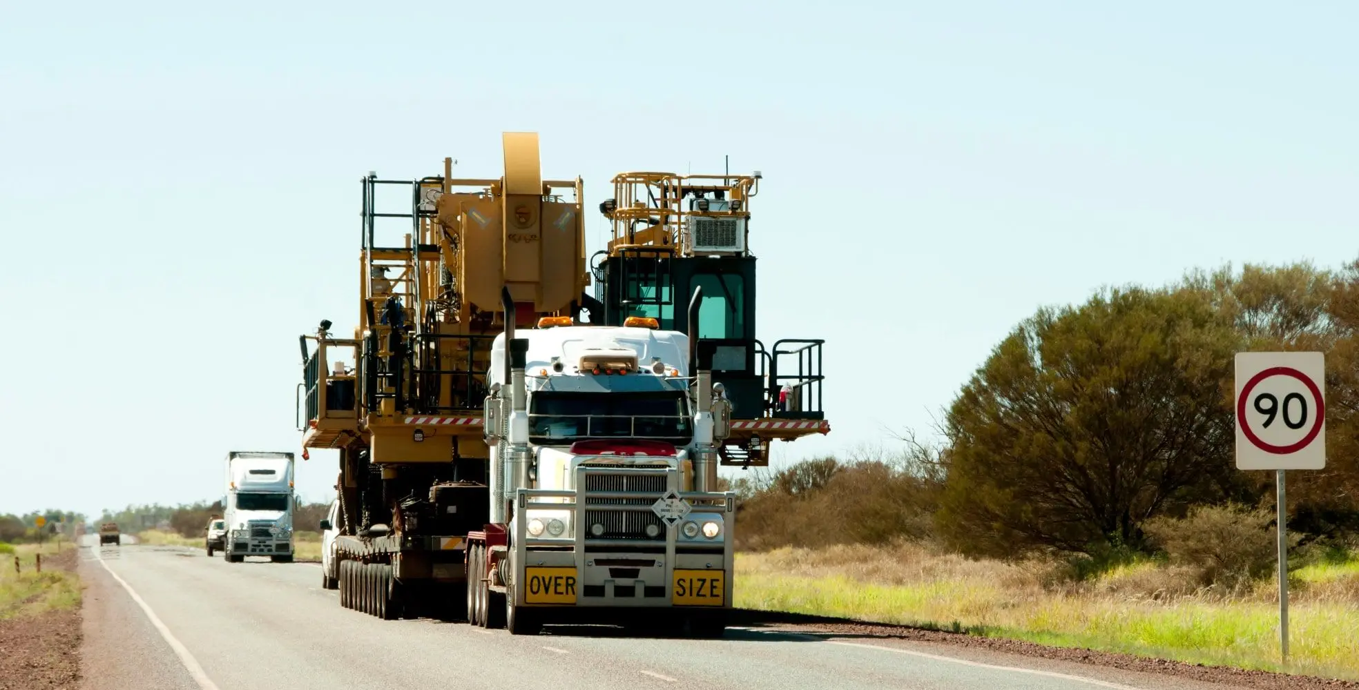 A truck carrying an oversized load of construction equipment down a street