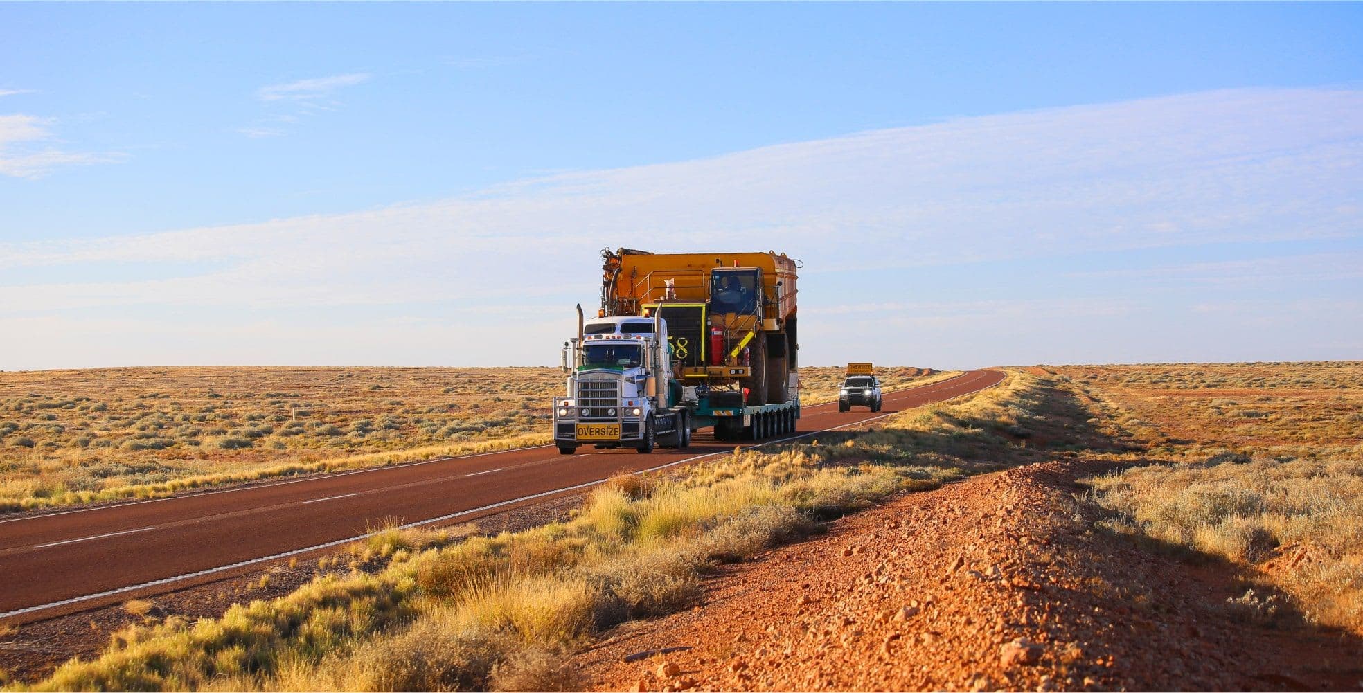truck hauling large construction equipment down a desert road